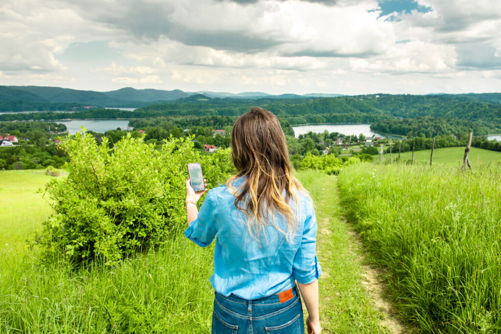 Kobieta trzymająca smartfon i korzystająca z rozszerzonej rzeczywistości w aplikacji turystycznej, która pokazuje najciekawsze miejsca w Bieszczadach